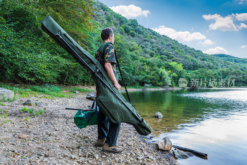 钓鱼历险，钓鲤鱼。湖边的渔夫，带着伪装的渔具，绿色的袋子和仿造的钓竿手提袋