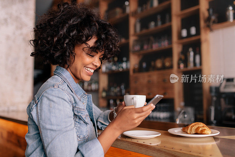 微笑的女人使用智能手机在一个现代的咖啡馆