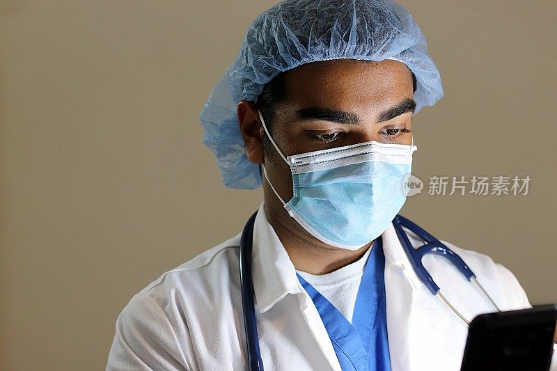 年轻英俊的医生穿着蓝色的手术服低头看手机