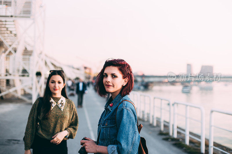 美丽的年轻女孩沿着河边的码头散步，一边聊天，一边拍照