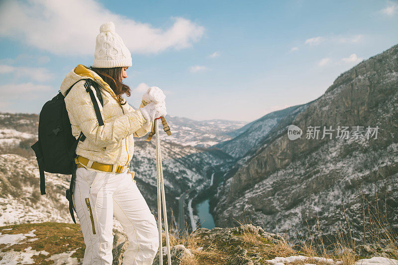 近景美丽的年轻女子在冬天的衣服站在一边，手拿木棍的背景雪山