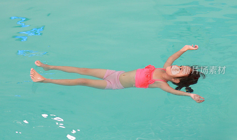 小女孩在游泳池的水面上漂浮着。