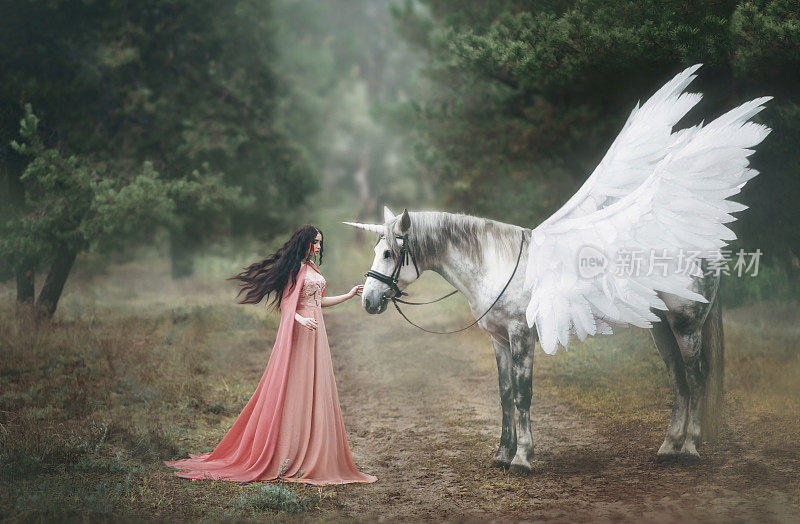 美丽年轻的精灵，与一只独角兽在森林里散步她穿着一件橙色长裙，披着斗篷。羽毛在风中美丽地飘动。艺术摄影