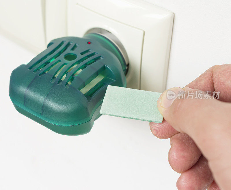 男人的手用电驱蚊板或熏蒸器插在插座上。电蚊香。有选择性的重点。