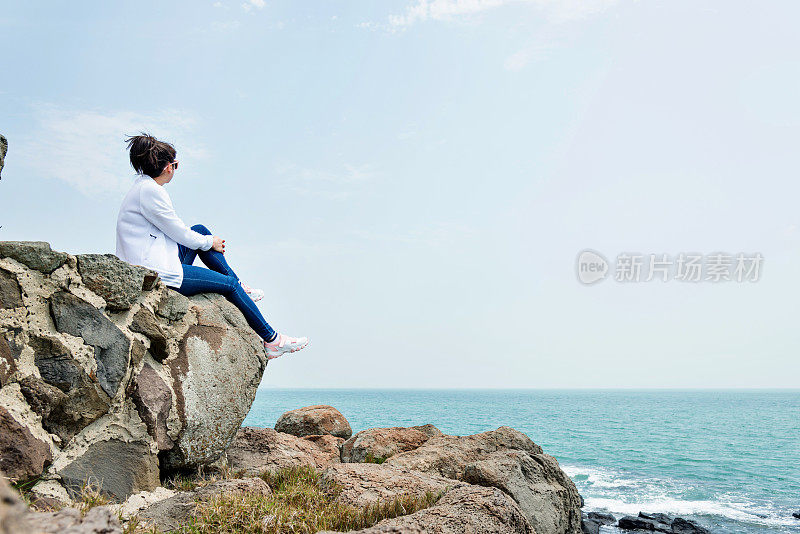 坐在海滩边岩石上的女人