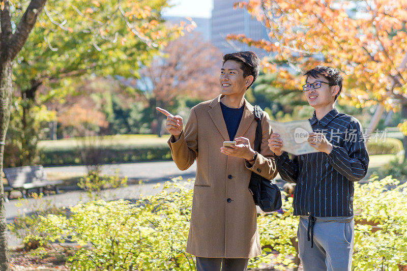 年轻的亚洲男子和日本朋友寻找旅游地点使用手机和花时间在亚洲旅行