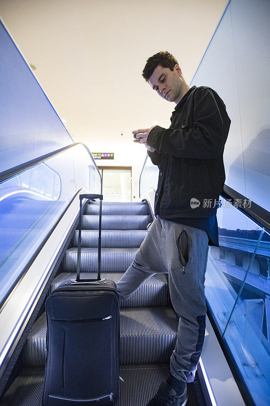 年轻成年男子在机场的自动扶梯上使用手机
