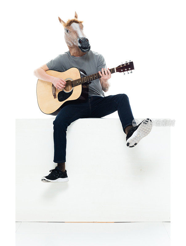 白人年轻男性吉他手坐在前面的白色背景穿着马服装和持有原声吉他