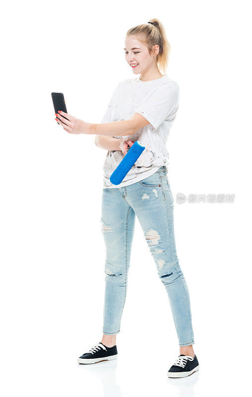 z一代少女画家穿着牛仔裤站在白色背景前使用手机