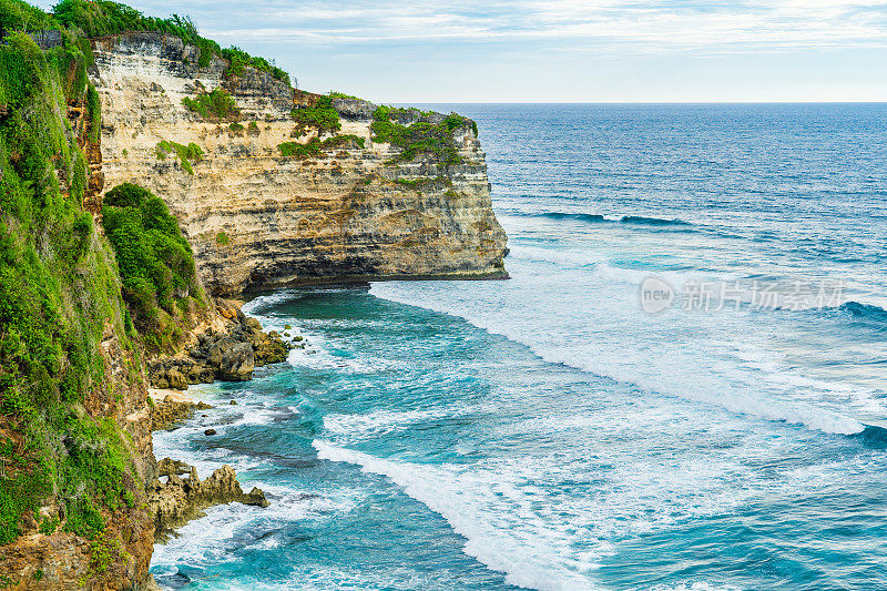 Uluwatu巴厘岛。蓝色的海洋和岩石山，覆盖着热带树木。