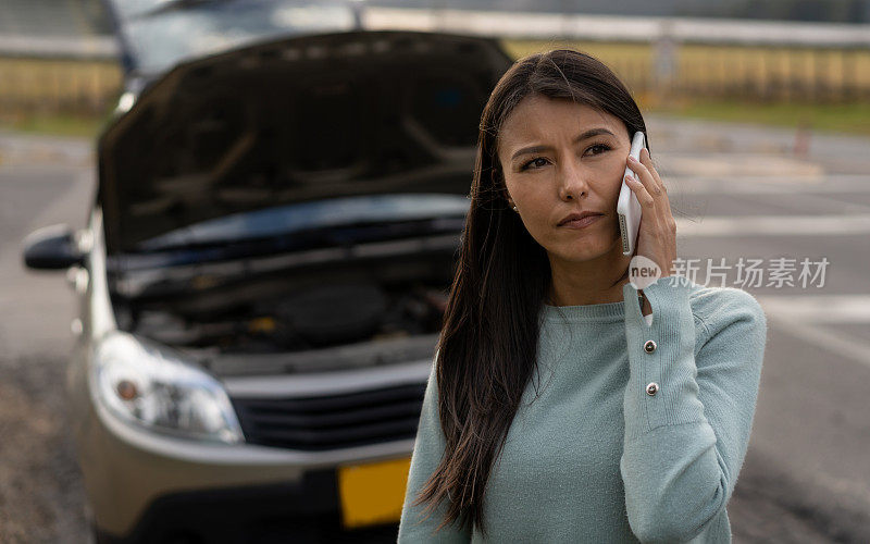 一位拉丁美洲妇女用智能手机呼叫路边救援，看起来很担心