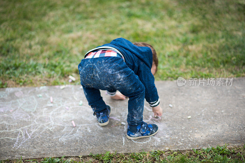 蹒跚学步的男孩，孩子，快乐地在户外玩，用粉笔在他的后院画画