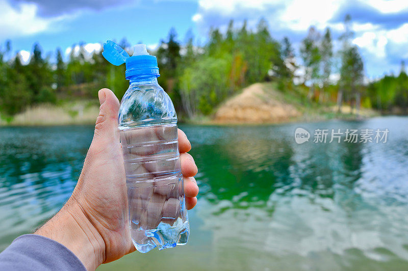 一名男子的手拿着一个水瓶，背景是绿松石色调的清澈湖水和夏日风景。