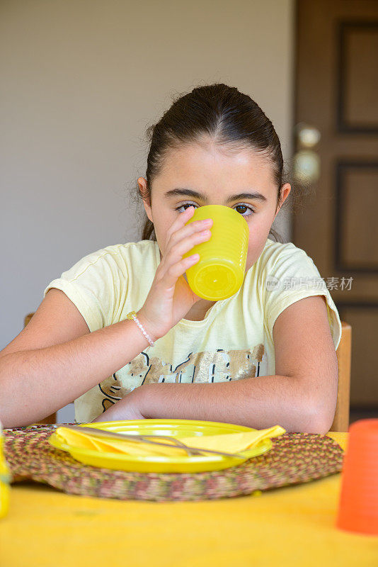 黄色的挑战。
一个小女孩用黄色杯子喝水的画像