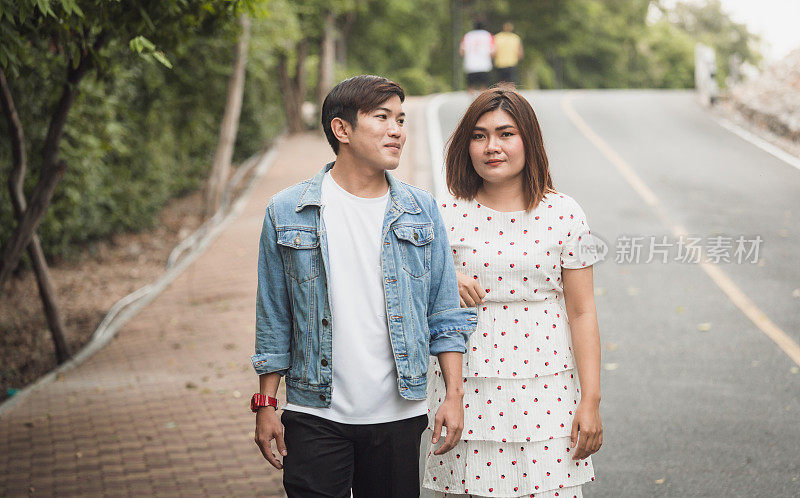年轻的亚洲情侣浪漫地一起在公园里散步