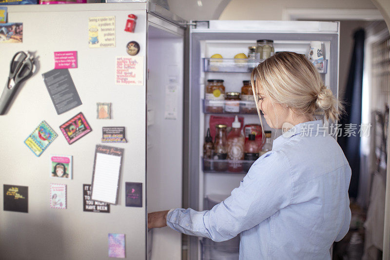 一个金发女人从冰箱里拿食物。