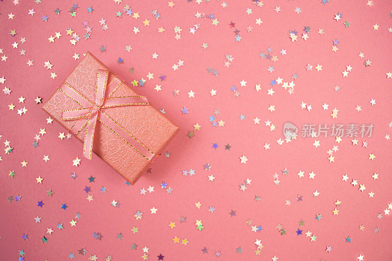 粉红礼盒与丝带和彩虹全息星星纸屑。粉彩背景上最小的平铺。