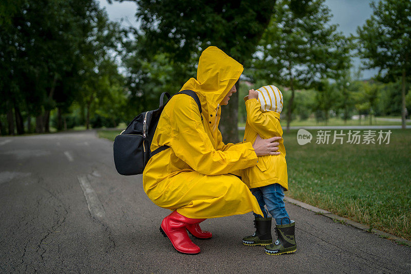 母亲和一个孩子。穿着雨衣的母子在公园里手牵着手