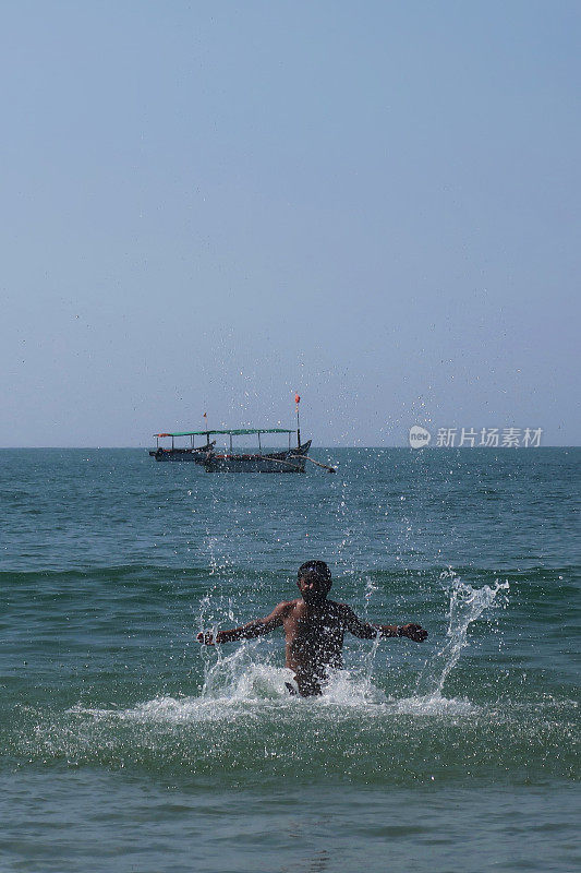 印度一名男子在海滩度假，站在齐腰深的水中，在印度洋中溅起水花，戴着护目镜，伸开双臂溅起水花，看起来很开心，印度果阿的帕洛伦海滩