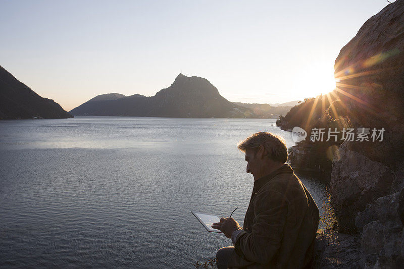 日出时分，一名男子在湖边使用数码平板电脑