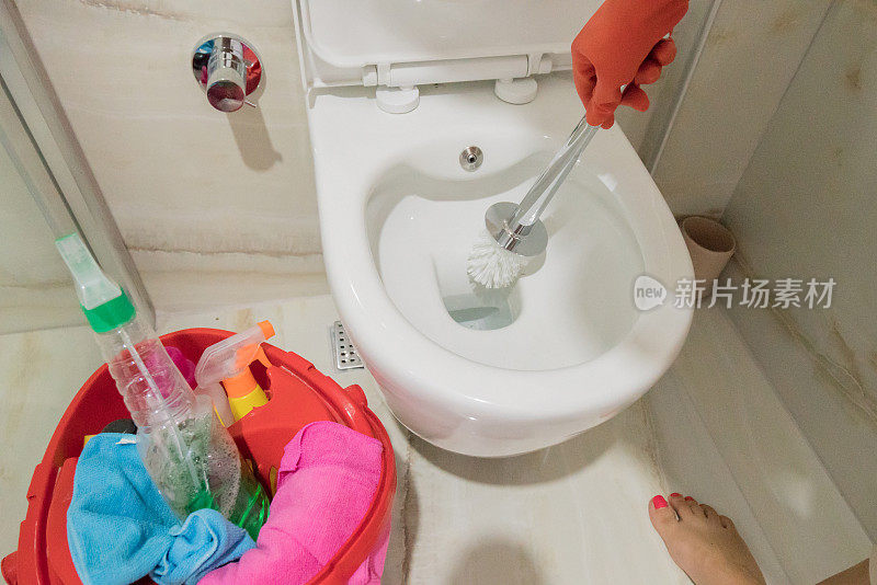 一位妇女正在用厕所刷和化学药品清洁她的浴室厕所。