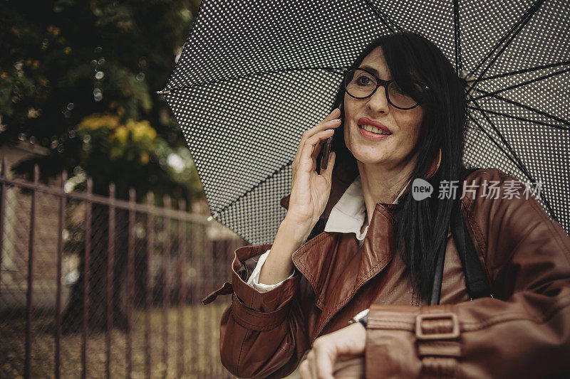 一位漂亮的商务老妇人在雨中行走，手里拿着手机