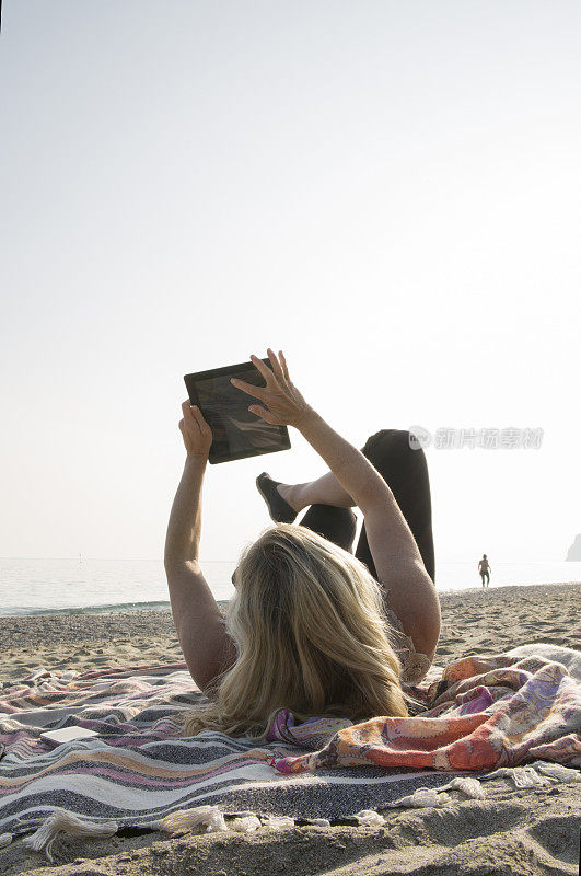 女人在沙滩上放松，用着平板电脑
