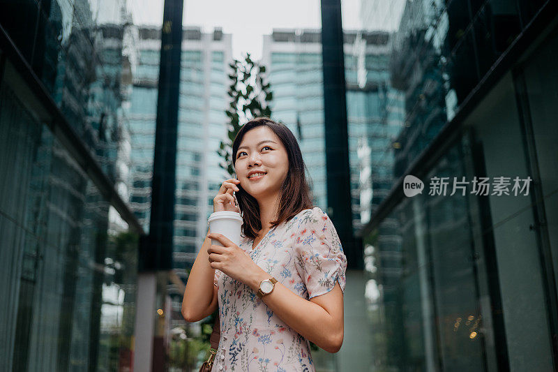 快乐的年轻亚洲女性使用智能手机和拿着纸咖啡杯