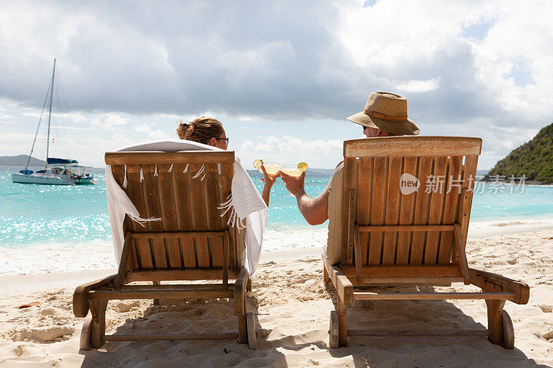 一对夫妇在热带海滩的柚木躺椅上喝着鸡尾酒敬酒