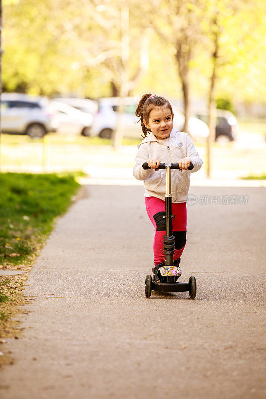 兴奋的小女孩在街上骑着她的推滑板车玩