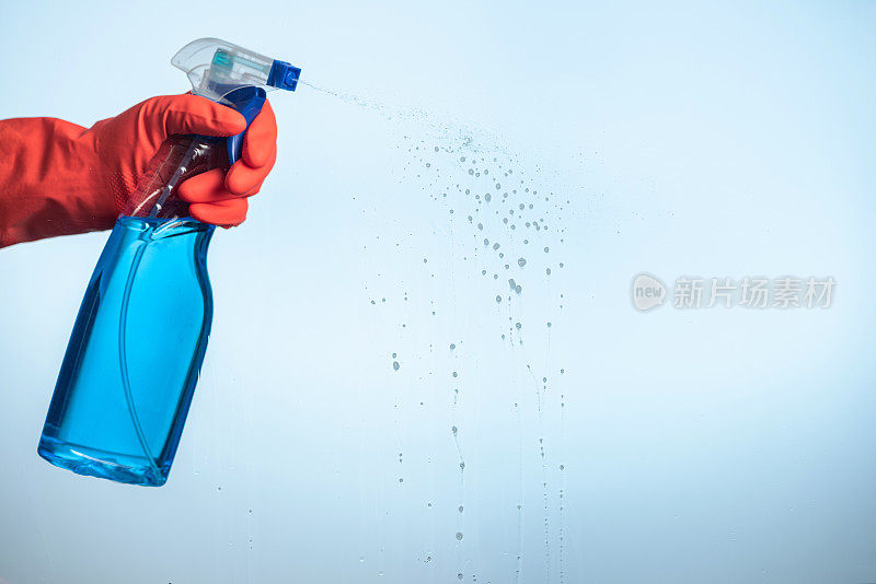 一只手拿着洗碗手套，将清洁剂喷洒在玻璃上。家居和汽车清洁服务的概念。