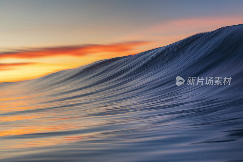 在温暖的日出海滩上形成平滑的波浪的特写