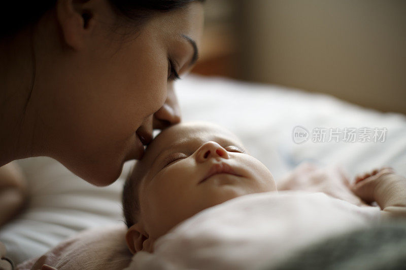 母亲亲吻她熟睡的新生婴儿