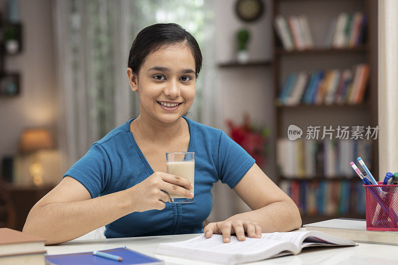 一个十几岁的女学生在家学习时喝牛奶的照片:库存照片