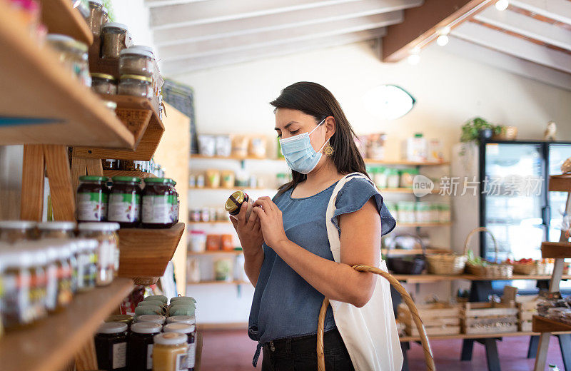 新常态:戴着防护口罩的年轻女性在当地的小商店购买有机食品