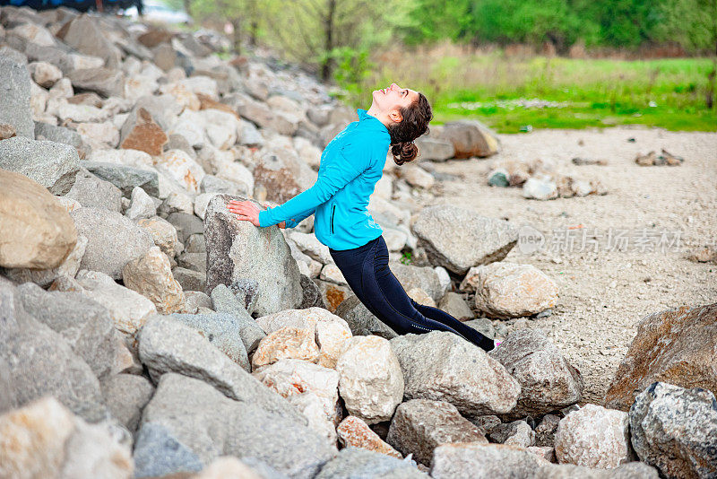 快乐的少女伸展在岩石堤岸上，向后弯腰