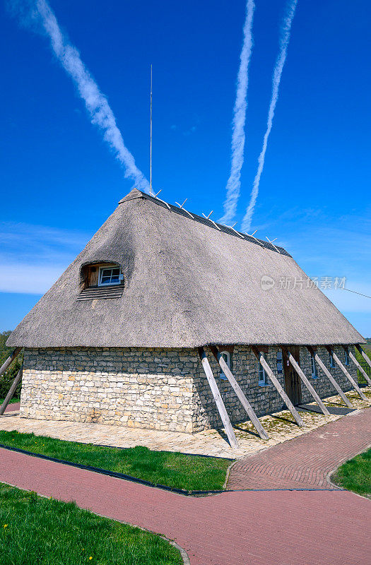 一个现代的老式房子，茅草屋顶，石头墙壁和支撑梁的两侧。前面是铺好的小路，背景是蓝色的天空。