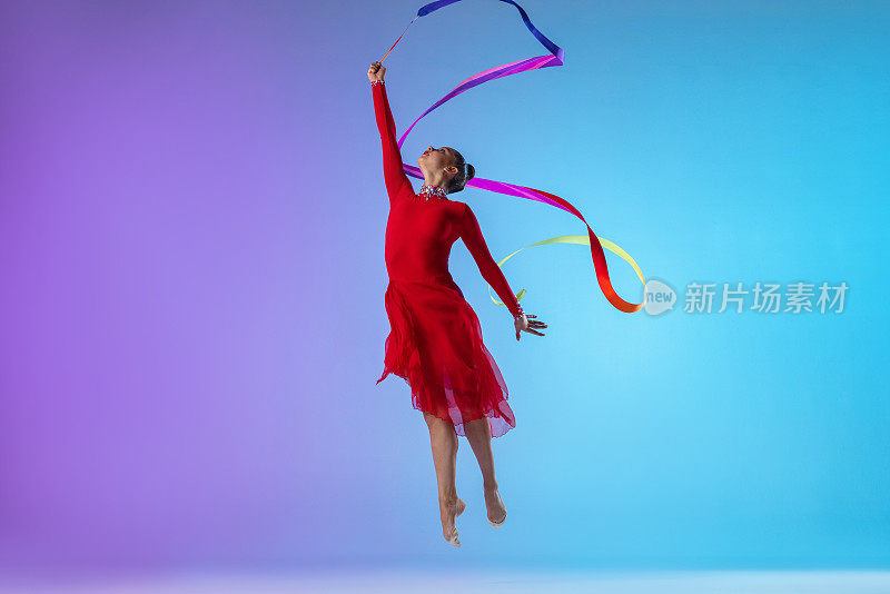 一名职业女艺术体操运动员，身着红色连衣裙，在霓虹灯的渐变背景下，用鲜艳的缎带分开运动。