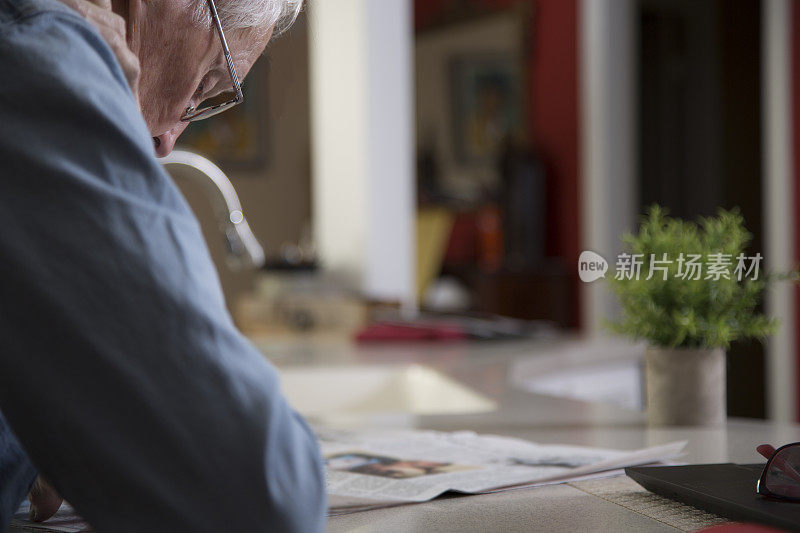 活跃的白人男子坐在厨房吧台上读晨报。他看完报纸后把它们回收利用。