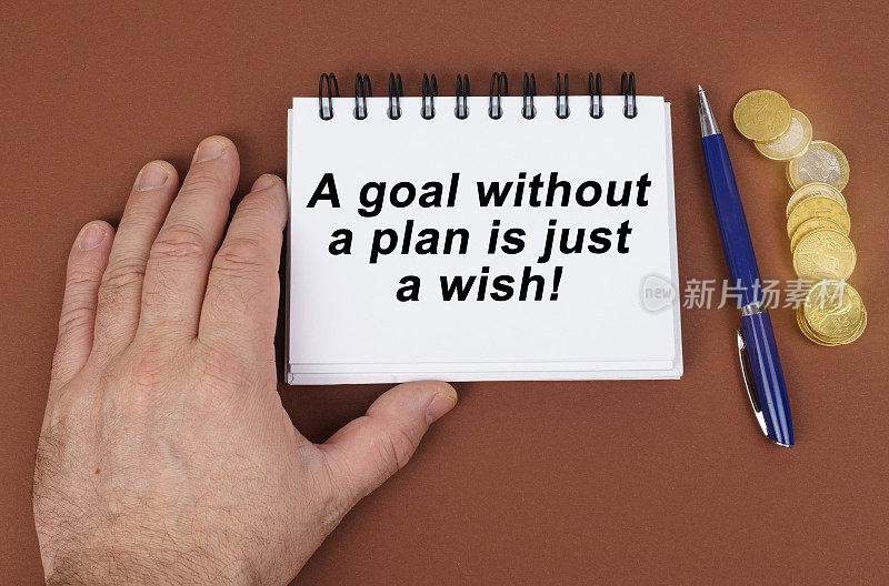 在棕色的表面是硬币，一支笔和一个写有文字的记事本——没有计划的目标只是一个愿望