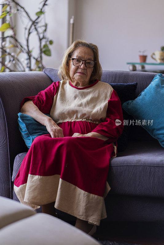 老奶奶坐在家里的沙发上，看着拍摄她的镜头