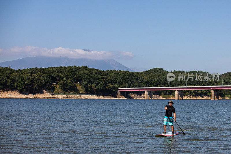阳光明媚的一天，男子在湖面上骑站立式桨板