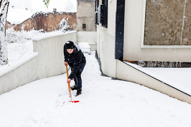 一个年轻人正在屋前用铲子清扫积雪。