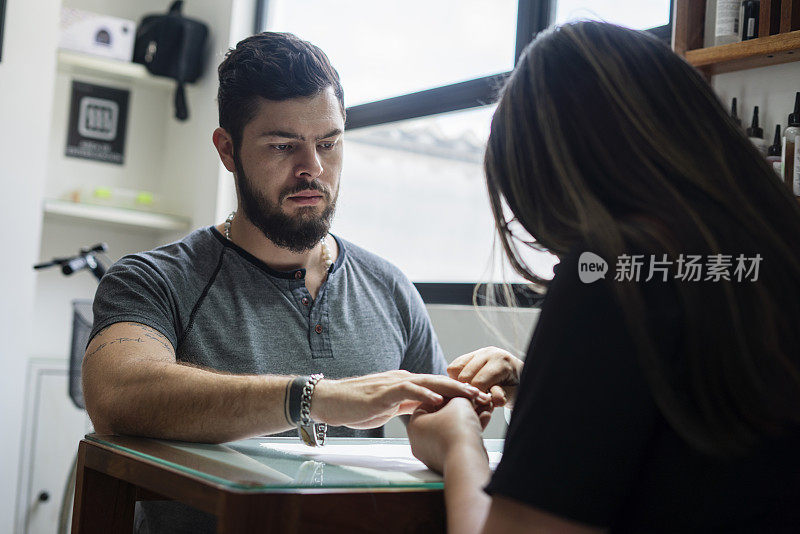 一名拉丁裔男子坐在发廊里，一名女美甲师正在为他做指甲