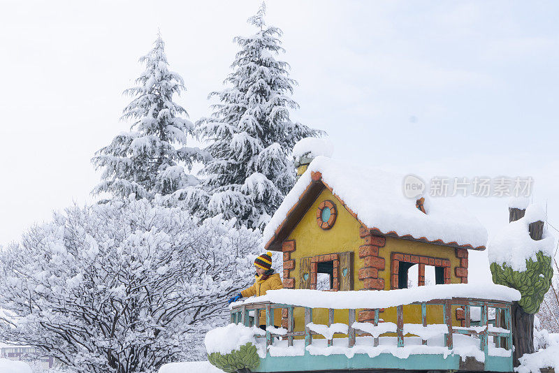 男孩在雪下的公共操场上玩树屋