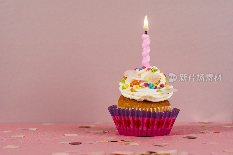 生日小蛋糕，粉色背景上有烛光。白色奶油蛋糕和糖果装饰。节日甜点，恭喜你。生日快乐。