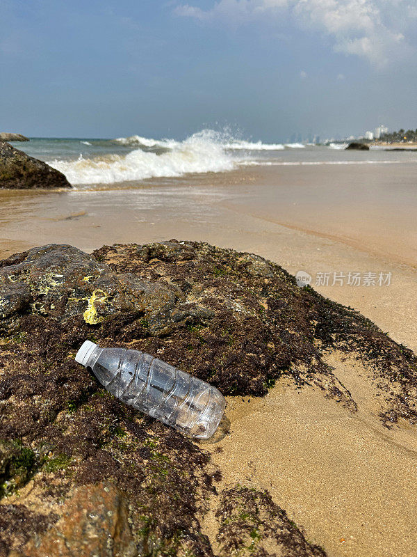 退潮时，白色盖子的透明空塑料水瓶被冲进岩石池，海岸上的海洋垃圾和污染，乱扔的沙子，肮脏的海滩，从拉维尼亚山海滩看到科伦坡市摩天大楼的海岸线