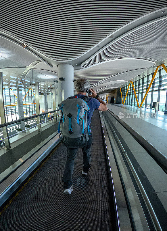 背包旅客在机场走廊的移动通道上登机。
