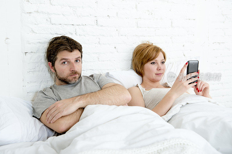 夫妻在床上丈夫沮丧的妻子使用手机
