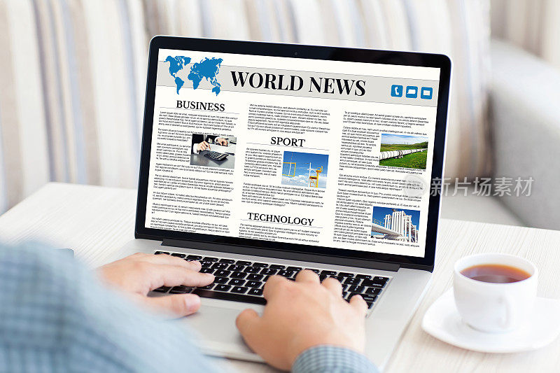 一名男子拿着笔记本电脑，屏幕上显示着世界新闻网站